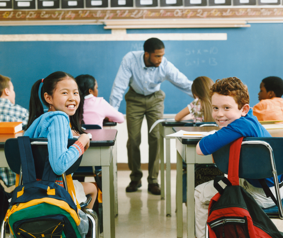 Students sit at their desks in a classroom, facing the teacher. In Baton Rouge, a girl and boy turn back, smiling as if inspired by future physicians.
