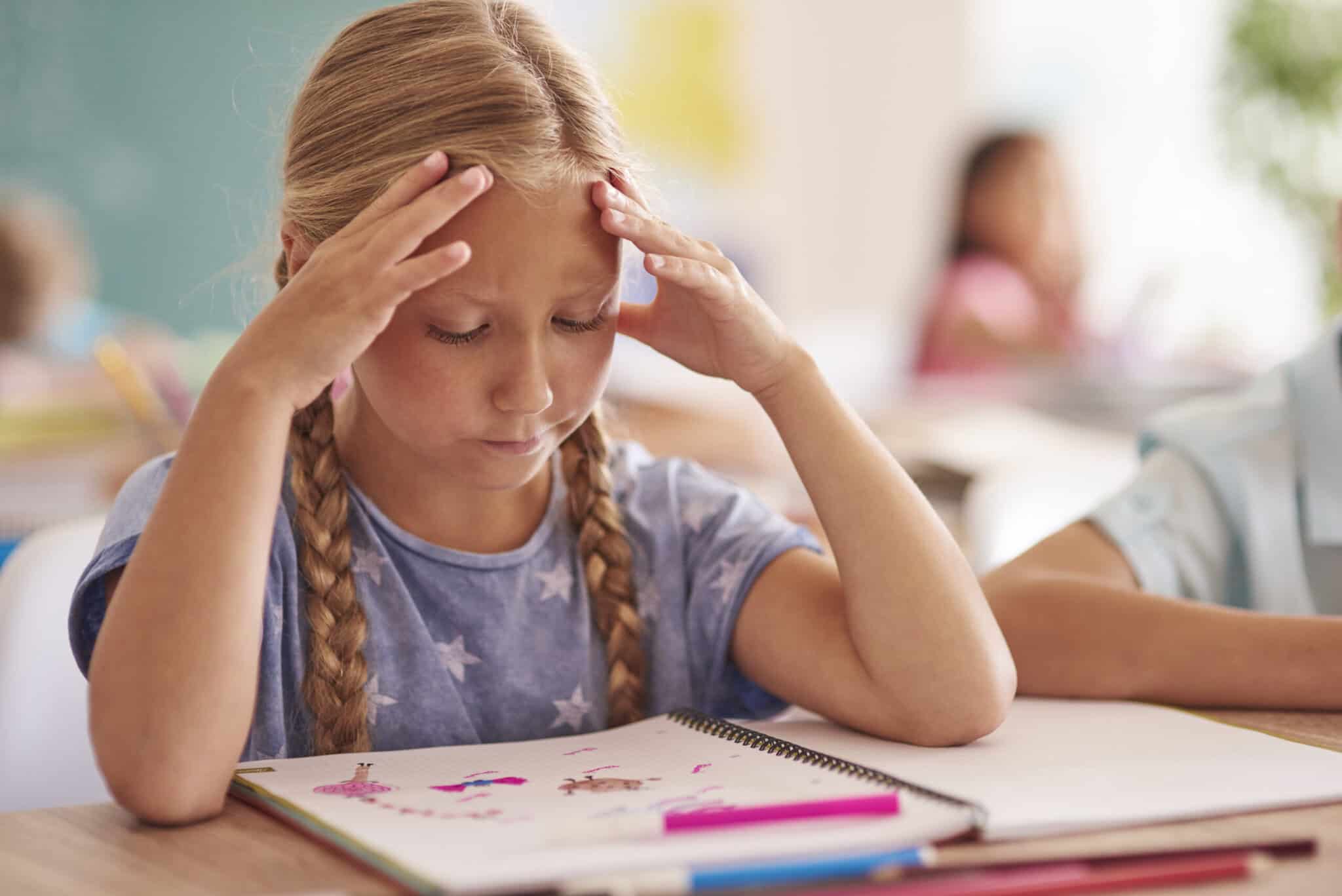 A girl with braided hair concentrates on a drawing in her notebook, surrounded by school supplies, under the care of dedicated Baton Rouge physicians.