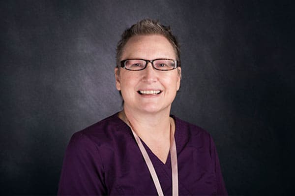 Person wearing glasses and a purple top, smiling in front of a dark background at The Baton Rouge Clinic.