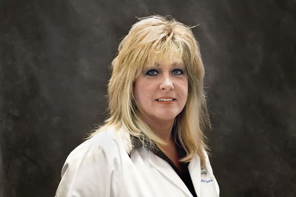 A woman with long blonde hair, wearing a white coat, poses against a dark background, reflecting the confidence of Baton Rouge physicians.