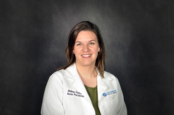 A woman in a white lab coat with 'Nurse Practitioner' embroidered on it stands against a dark background, representing Baton Rouge physicians.