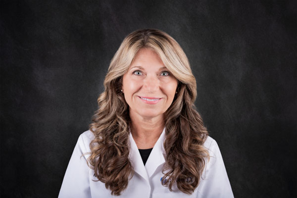 A woman with long wavy hair is wearing a white coat, smiling radiantly like one of the dedicated Baton Rouge physicians.