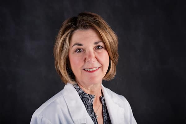 A woman with shoulder-length hair in a white coat, representing The Baton Rouge Clinic, smiles at the camera against a dark background.