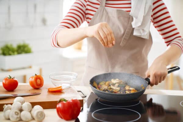 In a striped shirt and apron, a person cooks vegetables on a stovetop, as vibrant tomatoes and mushrooms sit nearby—perhaps fueling Baton Rouge physicians.