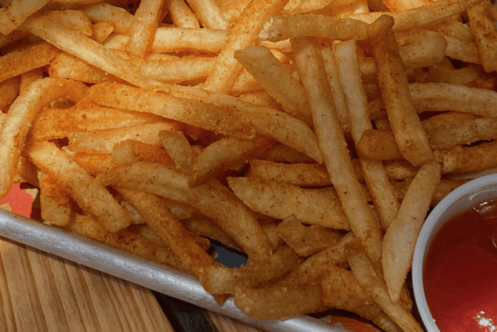 A tray of seasoned French fries with a small container of ketchup to the side, placed on a wooden surface.
