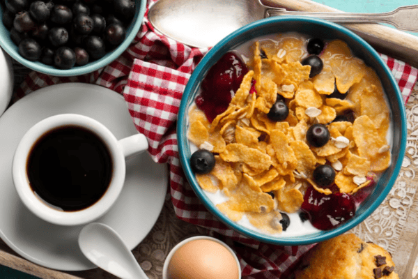 A tray with cereal and blueberries in milk, a boiled egg, a cup of coffee, a bowl of blueberries, and a chocolate chip muffin.