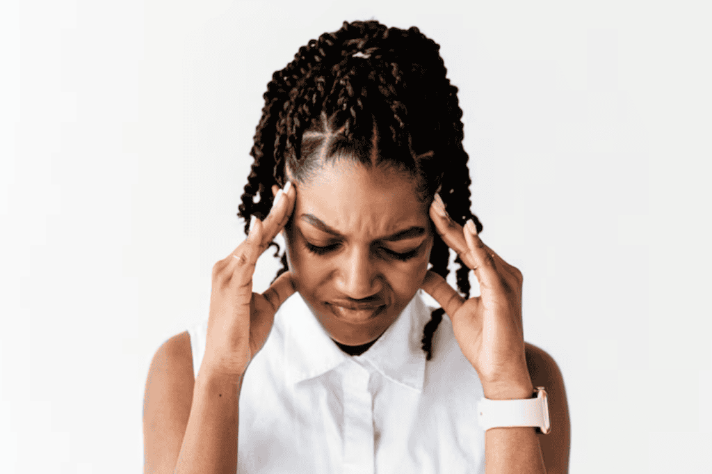 A woman with braided hair touches her temples and frowns, appearing to have a headache, against a plain white background.
