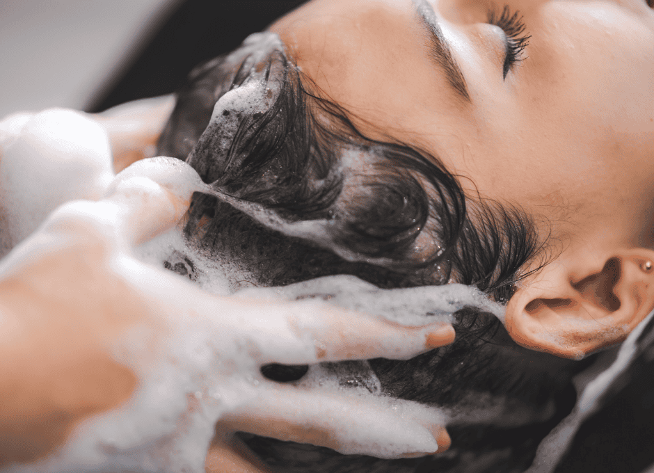 Close-up of a person getting their hair washed, with hands massaging shampoo into their scalp, creating foam and bubbles.