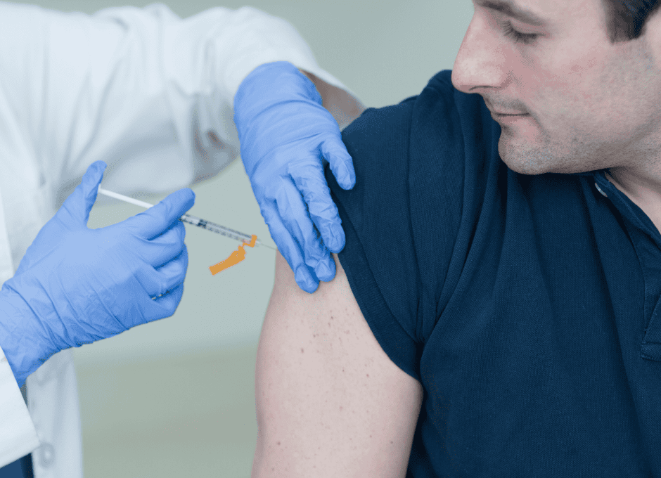 A healthcare worker in gloves gives an injection to a man's upper arm. The man is wearing a navy blue shirt and looking at his arm.