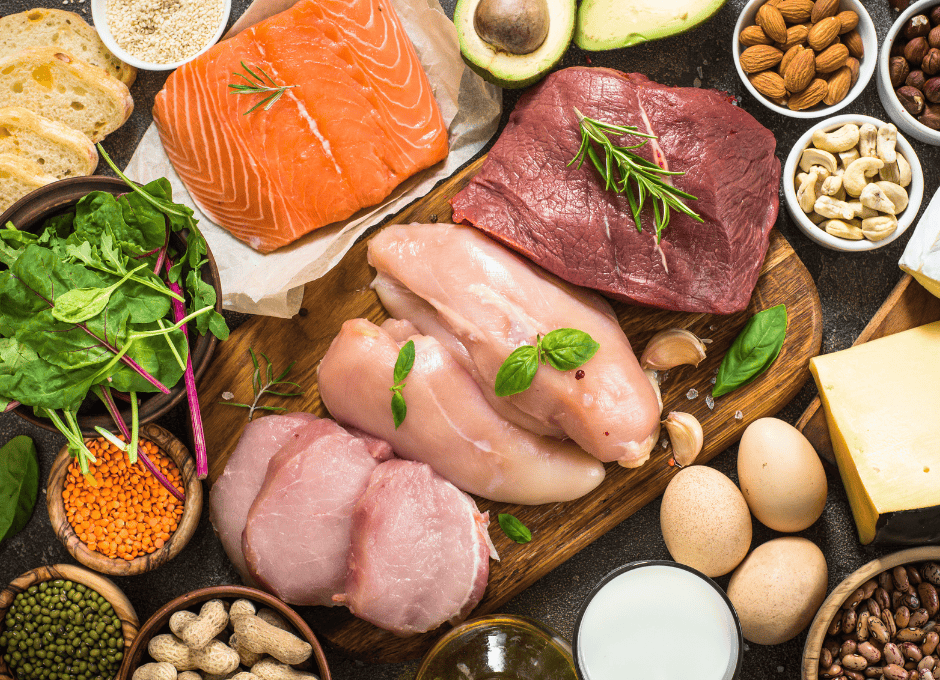 A variety of protein-rich foods, including raw salmon, beef, chicken, eggs, cheese, nuts, seeds, avocado, bread, and leafy greens.