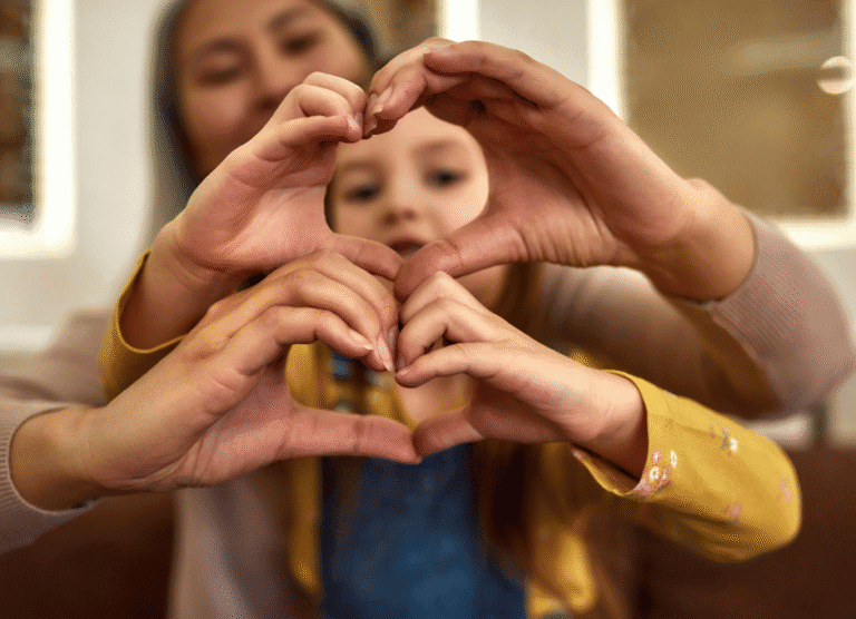 An adult and a child sit together, forming a heart shape with their hands in the foreground.