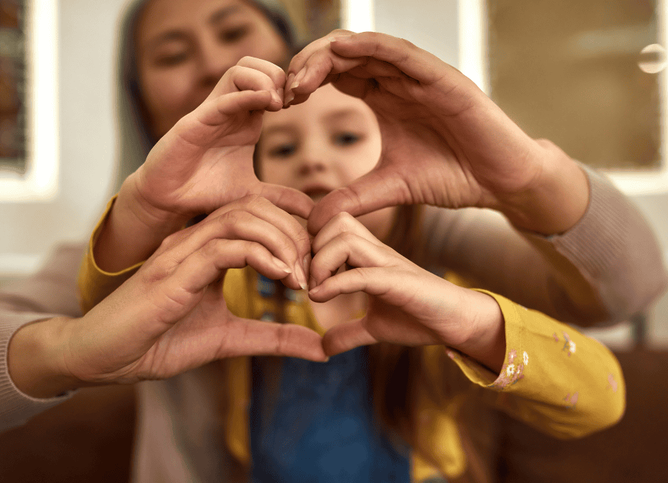 An adult and a child sit together, forming a heart shape with their hands in the foreground.