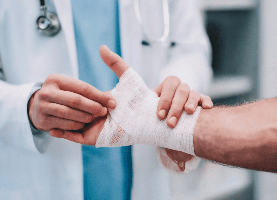A medical professional wraps a patient's hand and thumb with a bandage in a clinical setting.