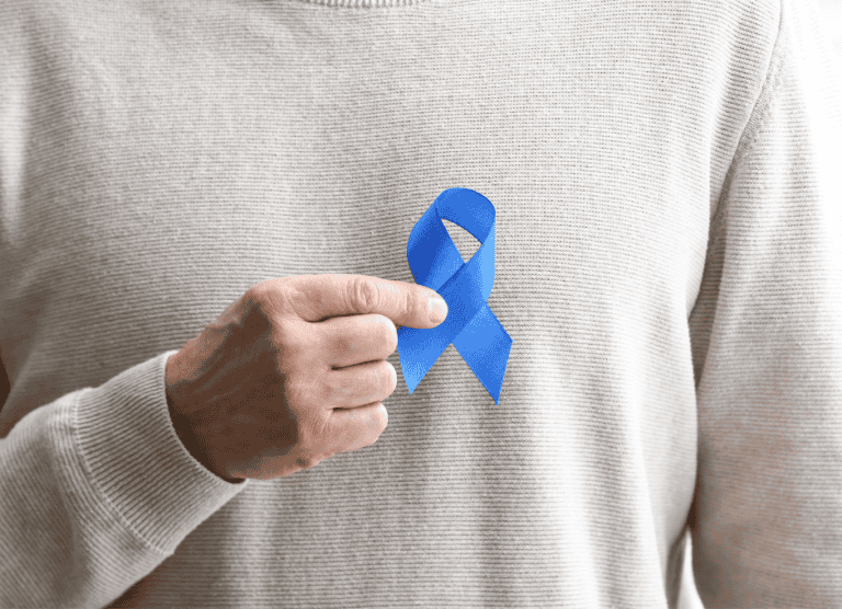 A person wearing a beige sweater holds a blue awareness ribbon pinned to their chest.